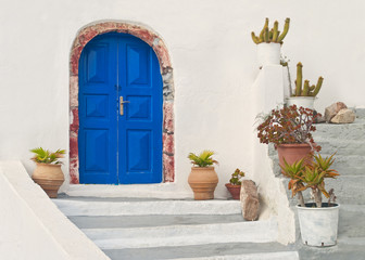 Fototapeta na wymiar white Greek house facade with blue door and flower pots