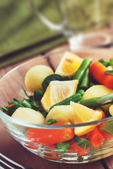 Salad with baby carrots, peas, onions and potatoes in glass bowl on wooden background