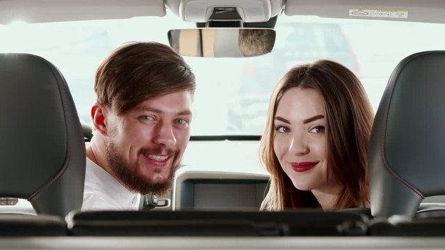 Attractive caucasian couple turning their faces to the back seat inside the car. Handsome man and pretty woman sitting on front seats. Young bearded guy and his girlfriend looking at each other