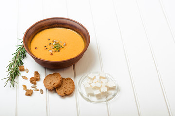 Pumpkin soup with bread crouton on white wooden table.