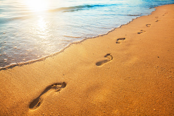 beach, wave and footprints at sunset time