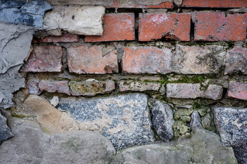 old rough ruined red brick wall with cement chunks and covered with moss