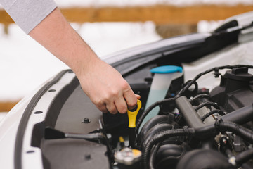 Fototapeta premium Car maintenance before winter. Man checking oil level in his car using dipstick. Outdoor closeup photograph