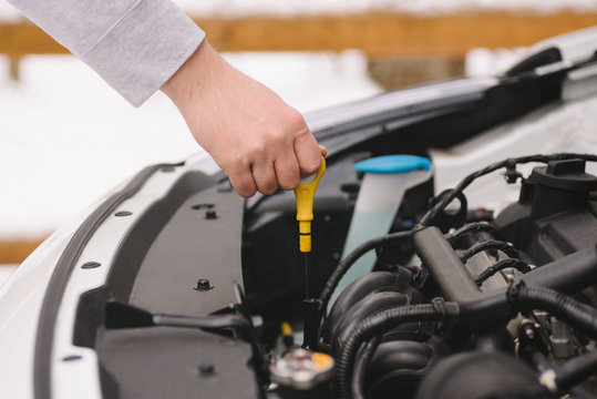 Car maintenance before winter. Man checking oil level in his car using dipstick. Outdoor closeup photograph