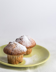 Two muffins by powdered sugar on green plate.