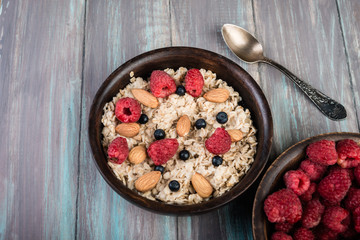  Healthy breakfast with homemade oatmeal with raspberry and nuts on rustic wooden background.