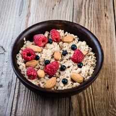  Healthy breakfast with homemade oatmeal with raspberry and nuts on rustic wooden background.