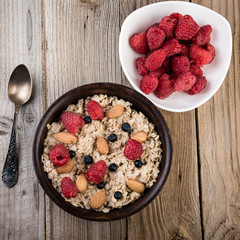  Healthy breakfast with homemade oatmeal with raspberry and nuts on rustic wooden background. Top view.