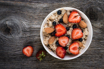 Oatmeal porridge with  blueberries, strawberries and muesli on wooden background. Top view. Diet breakfast.