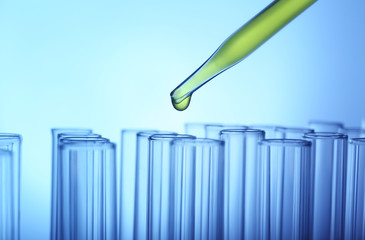 Closeup of a pipette dropping yellow sample into a test tube on light blue background