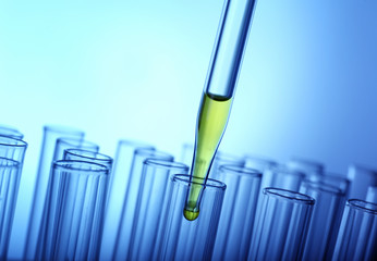 Closeup of a pipette dropping yellow sample into a test tube on light blue background