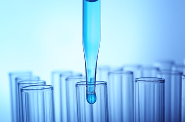 Closeup of a pipette dropping a sample into a test tube on light blue background