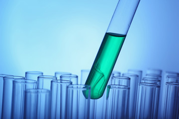 Test tube with green sample on light blue background