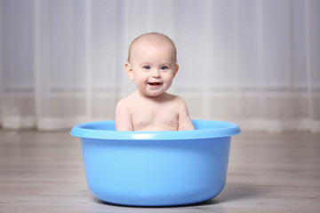 Cute baby in plastic basin at home