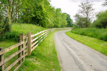 Fototapeta premium Country Road Lined with a Wooden Fence on a Cloudy Day