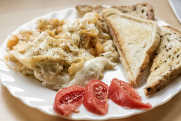 scrambled eggs with toasts and tomato on white plate