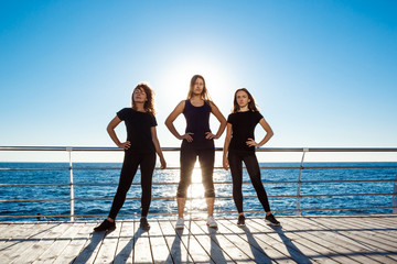 Silhouettes of sportive girls dancing zumba near sea at sunrise.