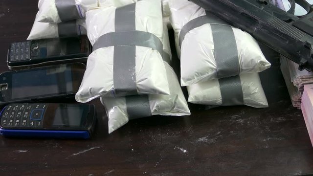 Seized drugs, money, gun, and burner phones on table