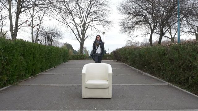 Woman walking into the park finds an armchair on an alee and rests in it