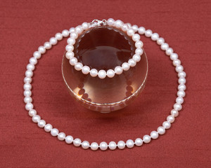 Freshwater white pearl necklace and crystal ball on red fabric background