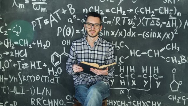 Young scientist man read book in chemical and mathematical equations wall room interior