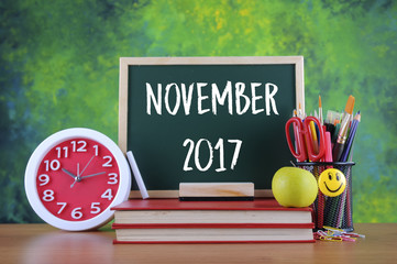 Back to school concept with alarm clock, books, a chalkboard and stationery with text NOVEMBER 2017