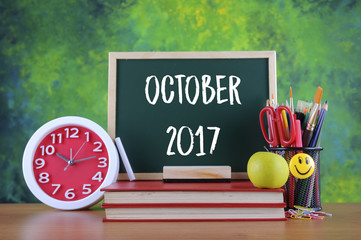 Back to school concept with alarm clock, books, a chalkboard and stationery with text OCTOBER 2017
