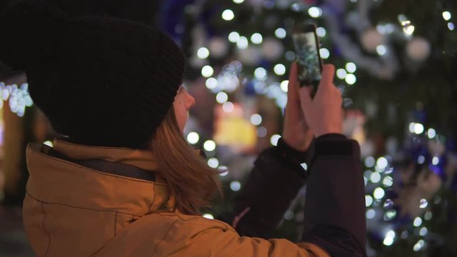 Young woman in bright winter clothes taking photo with mobile phone at the Christmas market