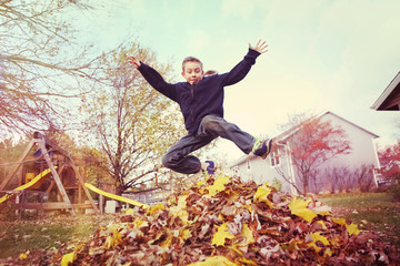 Boy jumping in a pile of autumn leaves