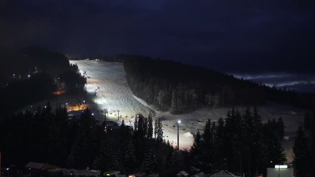 Night skiing and snowboarding at a ski resort and running ski lifts.