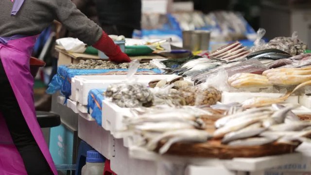 The seller puts the fresh seafood, mussels, oysters and fish on the counter. Traditional Asian market.