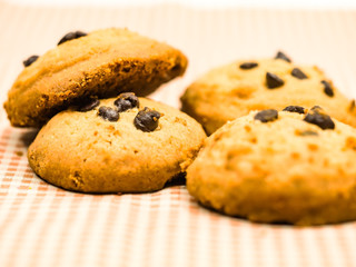 Stack of freshly baked chocolate chip cookies with glass of milk lying on linen napkin on rustic wooden table