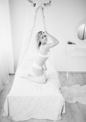 Curly blonde girl in underwear sitting on bed indoor white room.