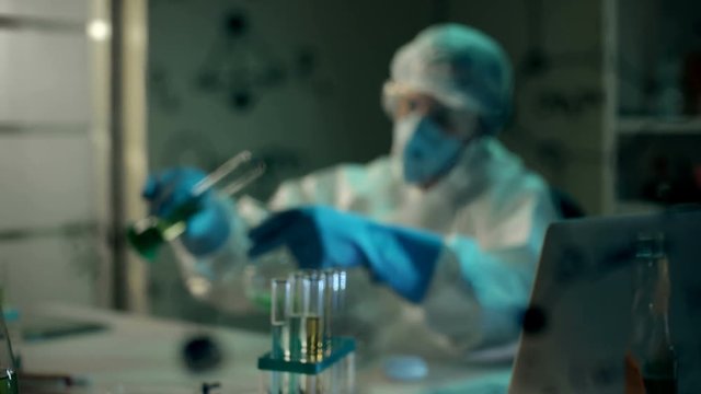 Crazy mad scientist in respirator drinks poisonous toxic liquid substance after performing an experiment in modern chemical laboratory. Development of a new drink. Joke in chemical lab