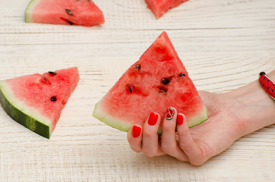 Triangular piece of watermelon in a female hand with a manicure on a light wooden background