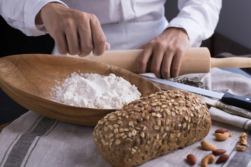 Whole grain bread put on kitchen napkin decorated with almond with a chef holding dough roller at the background.