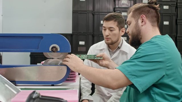 Technician teaching his male colleague how to work with PCB cutting machine