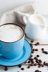 a cup of cappuccino and a milk jug on a white background