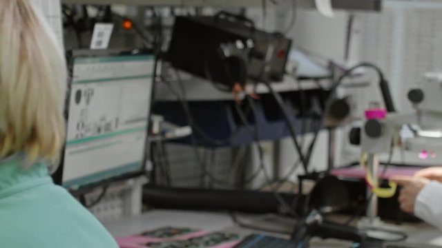 Tracking of women inspecting printed circuit board with microscope in laboratory