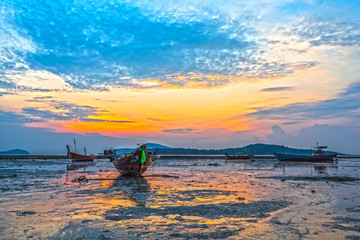 golden sky in Rawai beach fishing boats are parking on the mug 