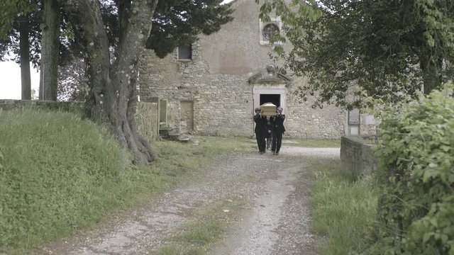 Pallbearers walking to graveyard with coffin followed by family