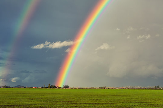 Big double rainbow over green field and red barn