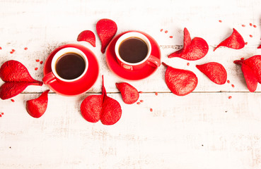 Two red coffee cups, petals in the shape of hearts on a white wooden background