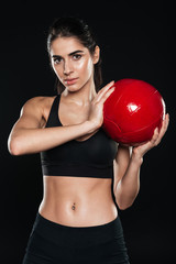 Concentrated sports woman holding fitness ball and looking at camera