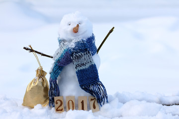 winter mood happy 2017/ merry snowman in a warm scarf holding bag with gifts on the background of a...