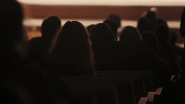 Spectators taking their seats in theater, view on dark hall and audience