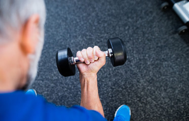 Unrecognizable senior man in gym working out with weights.