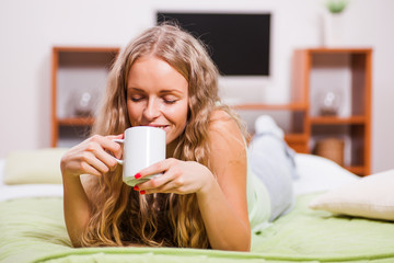 Young woman is lying in bed and drinking tea.