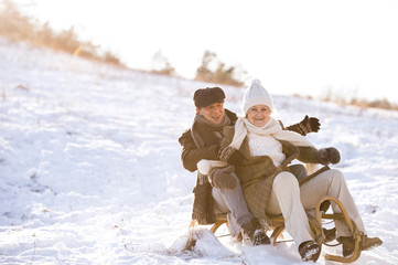 Beautiful senior couple on sledge having fun, winter day.