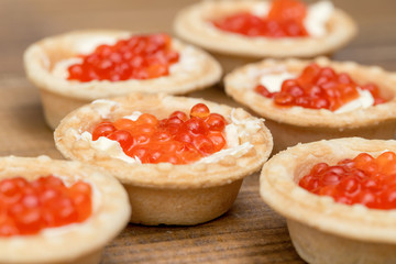 The Several tartlets with red caviar and butter on wooden brown table macro